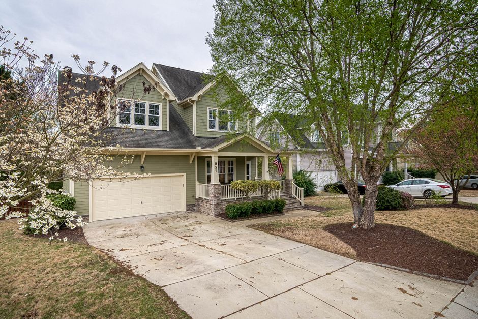 A picturesque suburban home with a lush front yard, driveway, and trees.